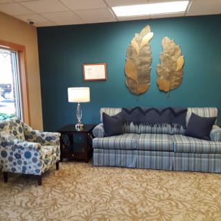 A cozy living room with a blue plaid couch, decorative pillows, a patterned armchair, and metallic wall art.
