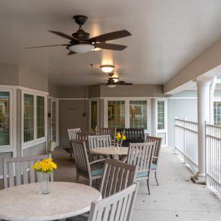 A covered patio with multiple tables and chairs, featuring ceiling fans and decorative flowers on each table.
