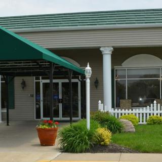 The entrance of a building featuring a green awning, columns, and landscaped surroundings.