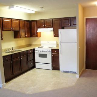 A compact kitchen with wooden cabinets, a stove, and a refrigerator in an apartment.