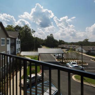 A view from a balcony overlooking a parking lot on a sunny day with clouds in the sky.