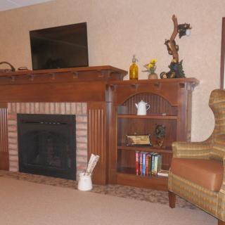 A cozy living room featuring a fireplace, bookshelf with decor, and an armchair.