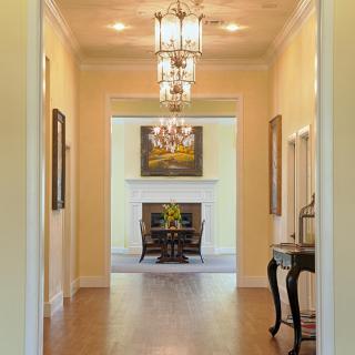 A well-lit hallway with elegant chandeliers leading to a cozy living area featuring a fireplace and artwork.