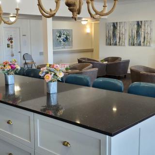 A modern kitchen with a dark countertop and floral decorations, overlooking a cozy living area.