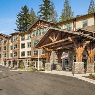 A modern multi-story building with a wooden entrance surrounded by trees.