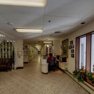 A well-lit hallway with a reception desk, seating area, and plants near the windows.