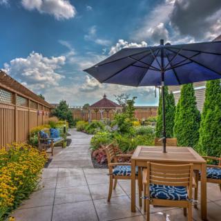 A beautiful garden patio with outdoor seating and an umbrella, surrounded by lush greenery and a pathway.
