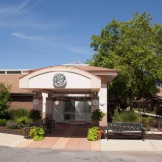 The front entrance of a building with landscaping and a bench.