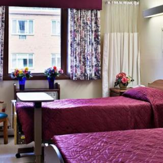 A hospital room with two beds and colorful curtains, featuring a bedside table with flowers.