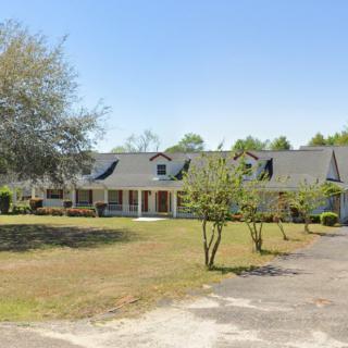 A spacious suburban home with a large lawn and driveway under a clear blue sky.