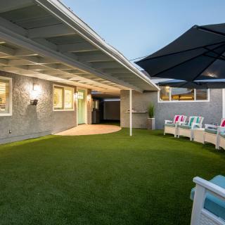 A cozy backyard patio with artificial grass, comfortable seating, and a large umbrella, perfect for evening relaxation.