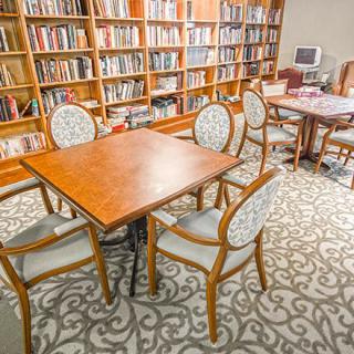 A cozy library reading area with tables, chairs, bookshelves, and a computer.