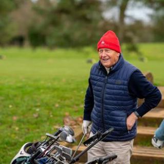 An elderly man enjoying a day on the golf course, wearing a bright red hat and a cozy vest.