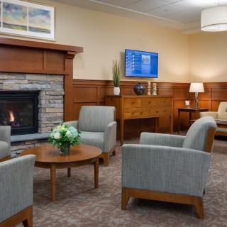 A cozy waiting room with comfortable chairs around a wooden coffee table, a warm fireplace, and tasteful decor.