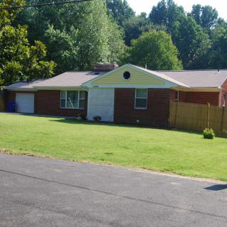 A suburban brick house with a well-maintained lawn and surrounding trees.