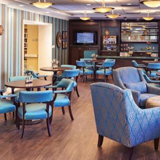 A modern lounge area featuring blue chairs, tables, and a bar with a wooden floor.