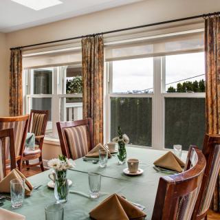 A well-set dining table in a bright room with large windows and elegant curtains.