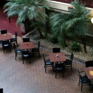 An indoor restaurant setting with empty tables and chairs, surrounded by lush plants and a brick floor.