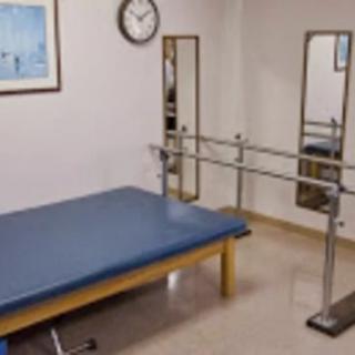 A physical therapy room equipped with a treatment table, parallel bars, and mirrors.