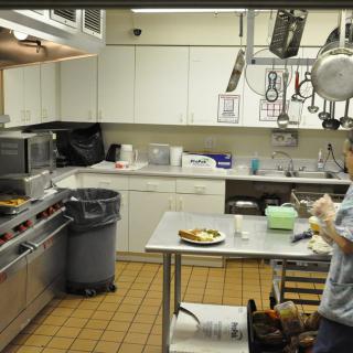 A commercial kitchen with a worker preparing food at a counter.
