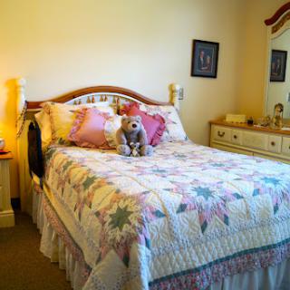 A cozy bedroom featuring a beautifully made bed with a quilt and a stuffed animal as decoration.