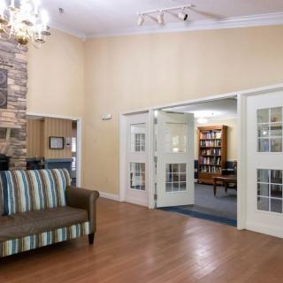A cozy lobby area featuring a striped sofa, wooden floors, and a bookshelf visible through open doors.