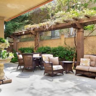 A cozy outdoor patio featuring comfortable seating under a wooden pergola, surrounded by lush greenery.