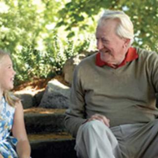 A young girl and an elderly man share a conversation on a park bench.