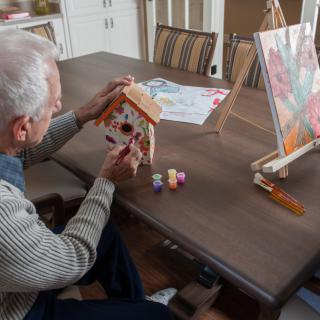 An elderly person painting a birdhouse as part of a creative activity.