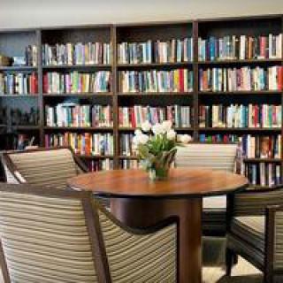 A cozy library corner featuring a round table surrounded by chairs, with bookshelves filled with books in the background.