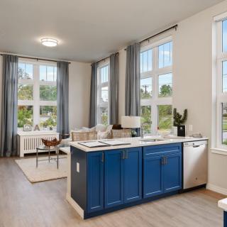 A modern open-concept kitchen and living area with blue cabinets and large windows letting in natural light.