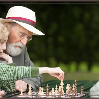 An elderly man and a young boy playing chess together in a park.