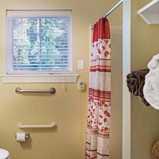 A bathroom with a window, patterned shower curtain, and accessible features.