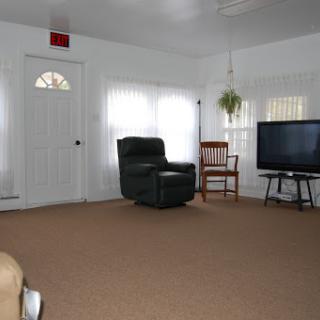 A cozy living room featuring a recliner, a small chair, a television, and natural light from the windows.