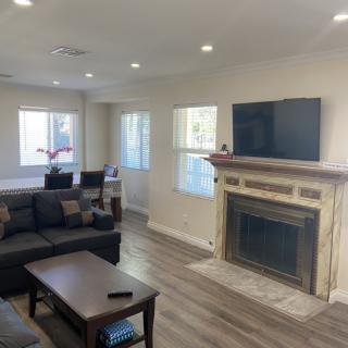 A cozy living room featuring a sofa, fireplace with a TV mounted above it, and a connected dining area.