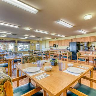 A spacious dining area with wooden tables and chairs, adjacent to a kitchen.