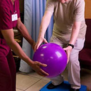 A therapist assists an elderly person with balance exercises using a stability ball.