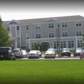 A residential building with a parking lot in front and a grassy lawn.