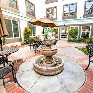 A charming courtyard featuring a central fountain surrounded by tables and chairs with umbrellas.