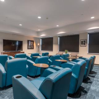 A comfortable lounge area with teal chairs arranged around a large television.