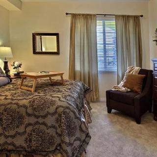 A cozy bedroom with patterned bedding, a comfortable chair, and a small table on the bed.