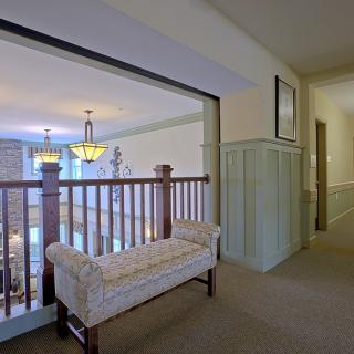 A hallway with a bench overlooking the stairs and well-lit interior.