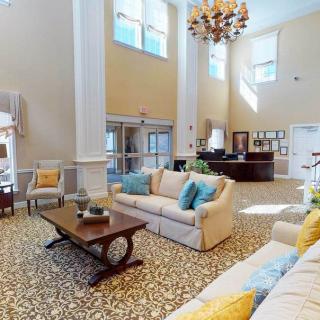 A spacious and elegantly decorated lobby with comfortable sofas, a central table, a large chandelier, and tall windows allowing natural light to fill the room.