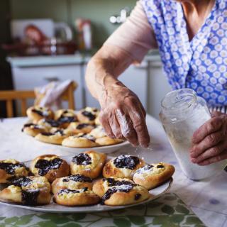 A person dusting powdered sugar over homemade pastries in a kitchen setting.