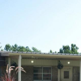 A single-story residential house with a front porch and surrounding greenery.