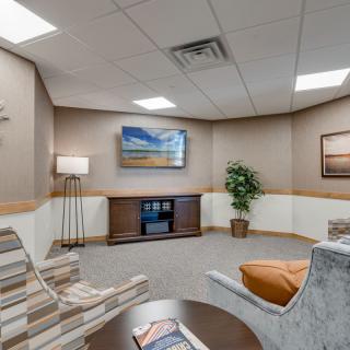 A comfortable waiting room with armchairs, a television, and decorative artwork.