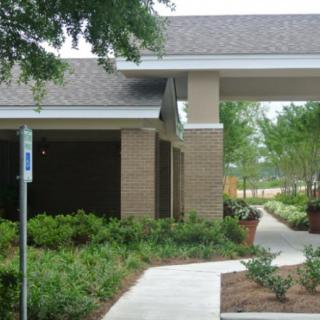 A building with a covered entrance surrounded by lush greenery and a paved walkway.