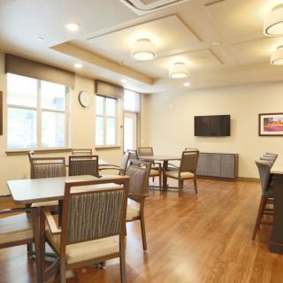 A modern dining room with wooden floors, featuring several tables and chairs, illuminated by stylish ceiling lights.
