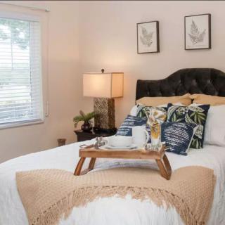 A cozy bedroom with a neatly made bed, decorated with pillows and a tray, alongside a bedside lamp.