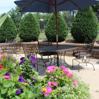 A beautifully arranged outdoor patio with colorful flowers, metal furniture, and a large umbrella.